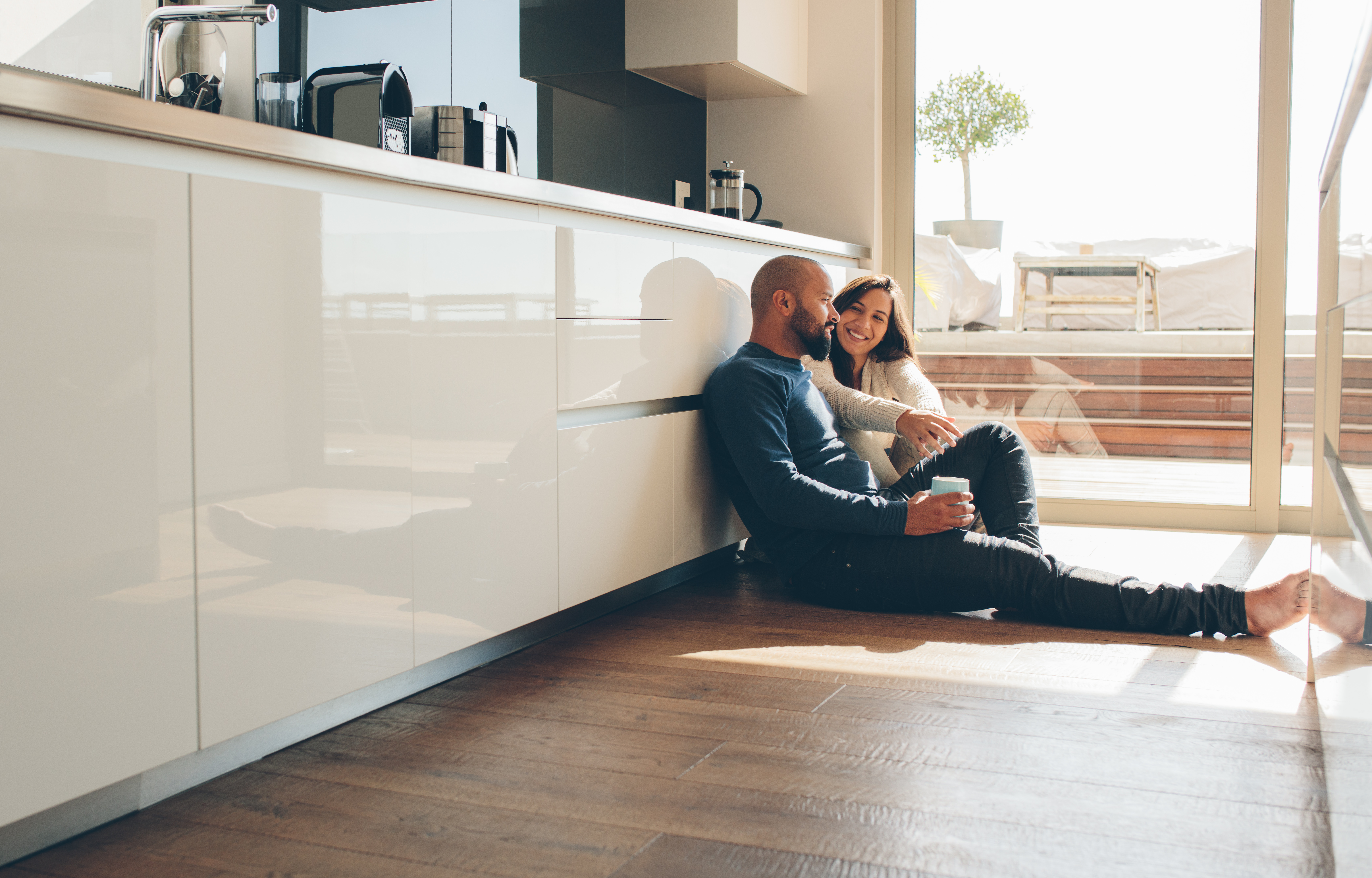 A couple sitting on their kitchen floor in front of their sink