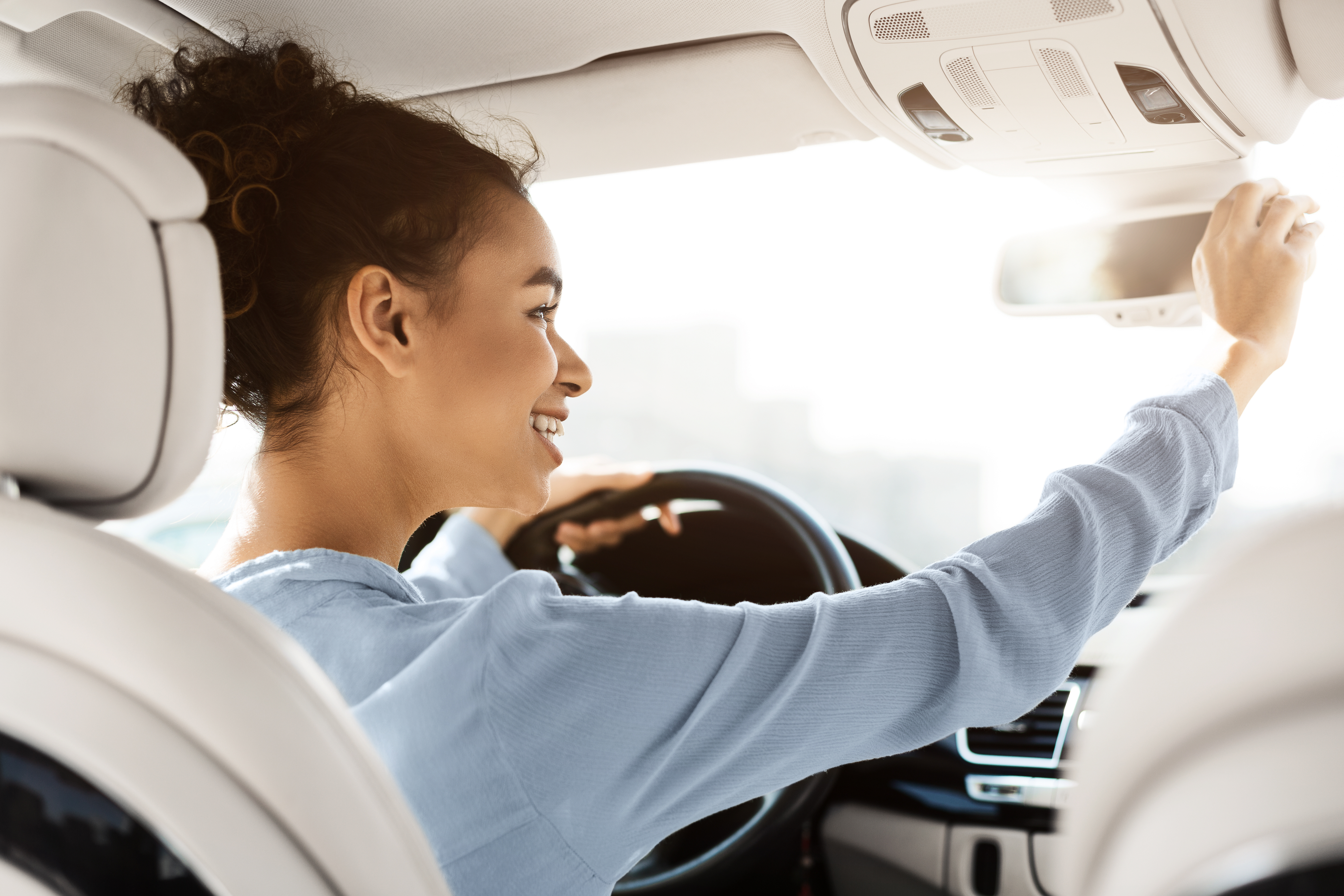 A woman adjusting her rearview mirror in her car